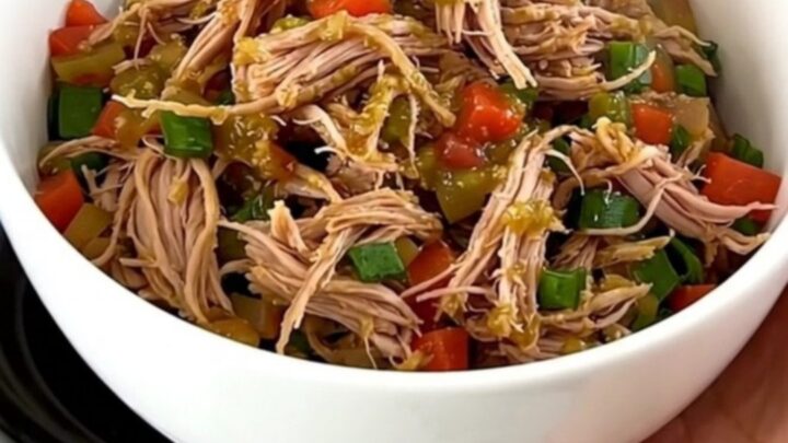 A close-up shot of a white bowl filled with slow-cooked shredded pork, black beans, and corn, topped with salsa verde.