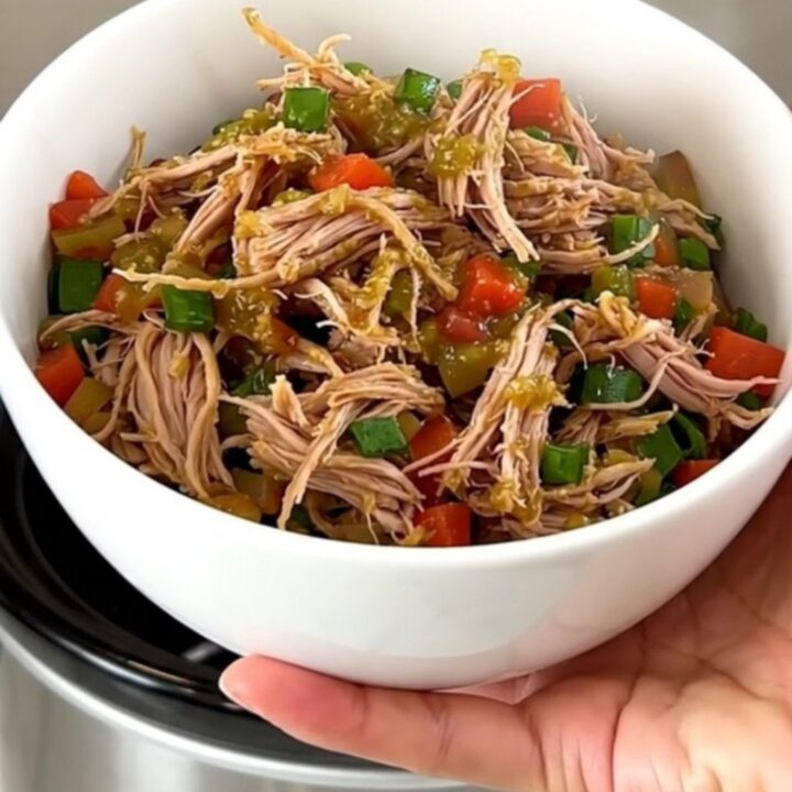 A close-up shot of a white bowl filled with slow-cooked shredded pork, black beans, and corn, topped with salsa verde.