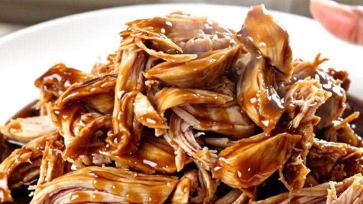 A top-down view of raw chicken breasts and aromatics being added to a slow cooker.