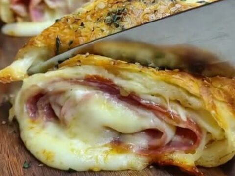A golden-brown Italian stromboli on a wooden board with molten cheese and cured meats visible in the cross-section.