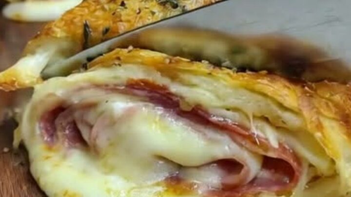A golden-brown Italian stromboli on a wooden board with molten cheese and cured meats visible in the cross-section.