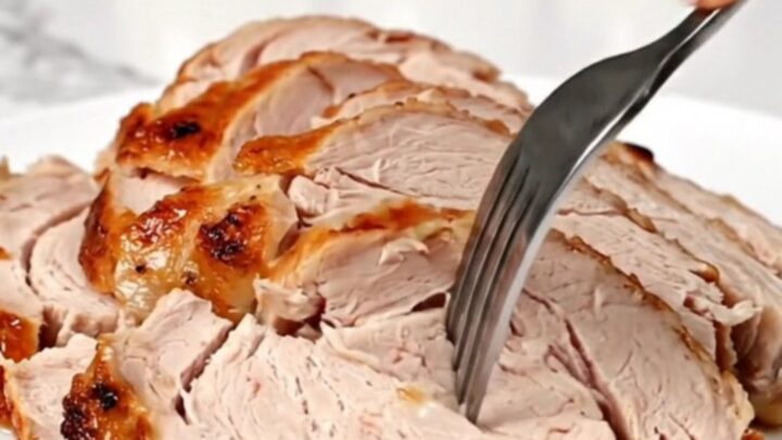 A juicy, sliced turkey breast on a round white plate with a blurred kitchen background.