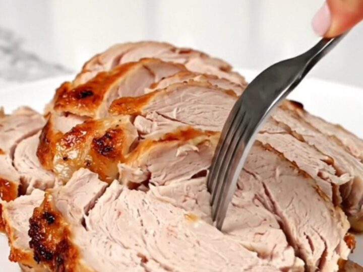 A juicy, sliced turkey breast on a round white plate with a blurred kitchen background.