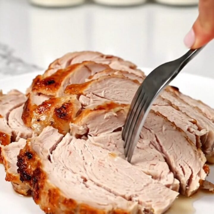 A juicy, sliced turkey breast on a round white plate with a blurred kitchen background.