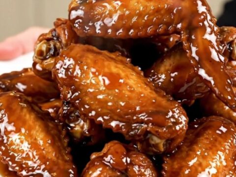 A plate of glossy, dark brown bourbon glazed chicken wings garnished with sliced green onions.