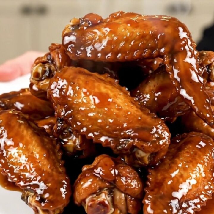 A plate of glossy, dark brown bourbon glazed chicken wings garnished with sliced green onions.