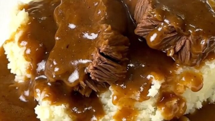 A close-up of tender beef tips in a rich mushroom gravy served over creamy mashed potatoes on a white plate.