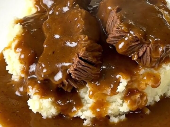 A close-up of tender beef tips in a rich mushroom gravy served over creamy mashed potatoes on a white plate.