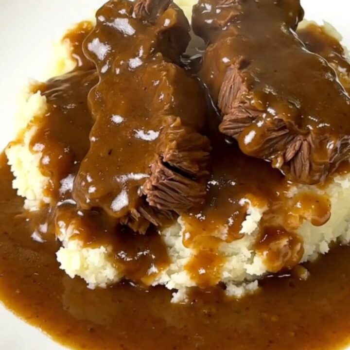 A close-up of tender beef tips in a rich mushroom gravy served over creamy mashed potatoes on a white plate.
