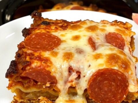 A top-down view of a black slow cooker filled with layers of sausage, pepperoni, and sauce.