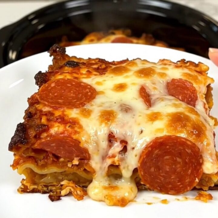 A top-down view of a black slow cooker filled with layers of sausage, pepperoni, and sauce.