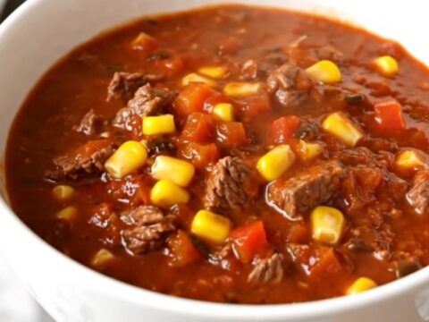 A steaming bowl of rich beef and poblano chili in a white bowl on a wooden table.