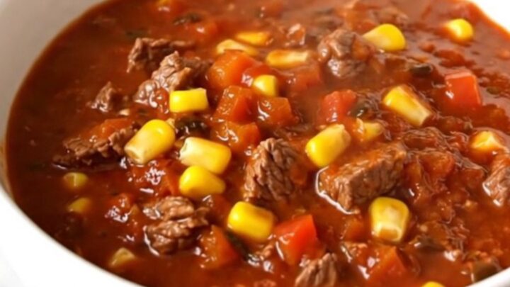 A steaming bowl of rich beef and poblano chili in a white bowl on a wooden table.