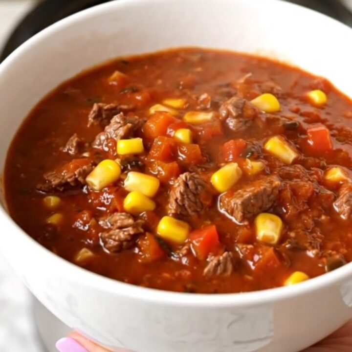 A steaming bowl of rich beef and poblano chili in a white bowl on a wooden table.