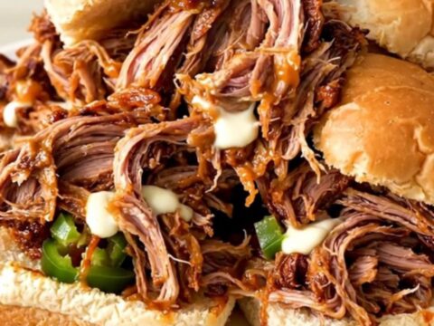 A close-up of a slow cooker filled with shredded pork, cream cheese, and diced jalapenos.