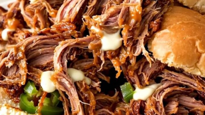 A close-up of a slow cooker filled with shredded pork, cream cheese, and diced jalapenos.