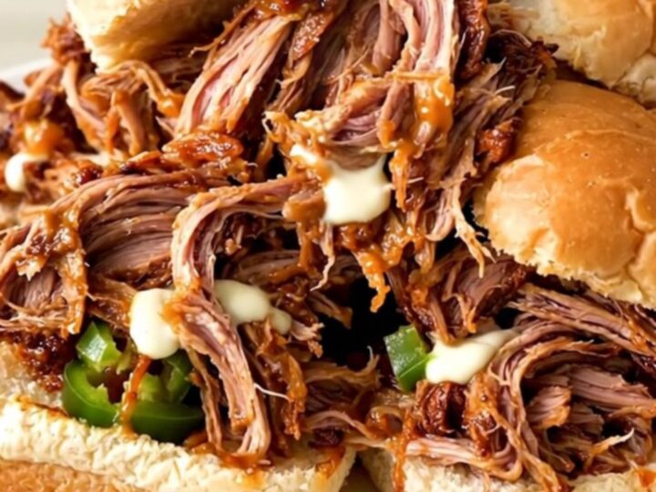 A close-up of a slow cooker filled with shredded pork, cream cheese, and diced jalapenos.