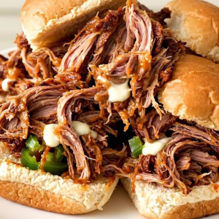 A close-up of a slow cooker filled with shredded pork, cream cheese, and diced jalapenos.