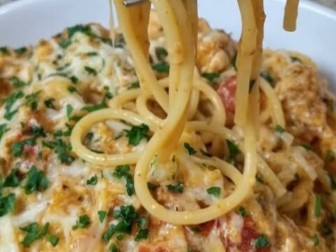 A close-up of creamy Rotel chicken spaghetti on a white plate with melted cheese strings.
