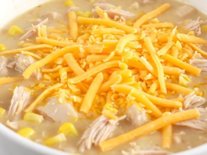 A steaming bowl of creamy chicken and corn chowder topped with melted cheddar cheese.