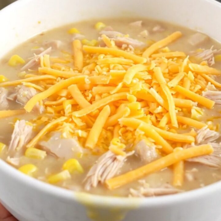 A steaming bowl of creamy chicken and corn chowder topped with melted cheddar cheese.