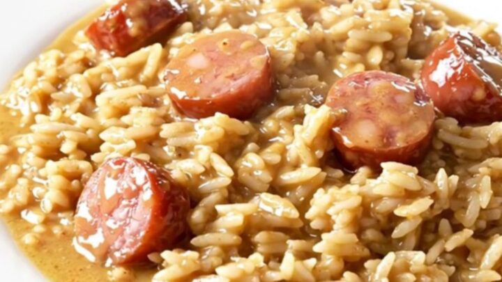 A close-up of a creamy Tuscan kielbasa and rice dish in a slow cooker on a white quartz countertop.