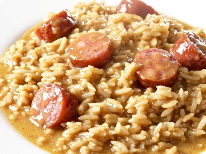 A close-up of a creamy Tuscan kielbasa and rice dish in a slow cooker on a white quartz countertop.