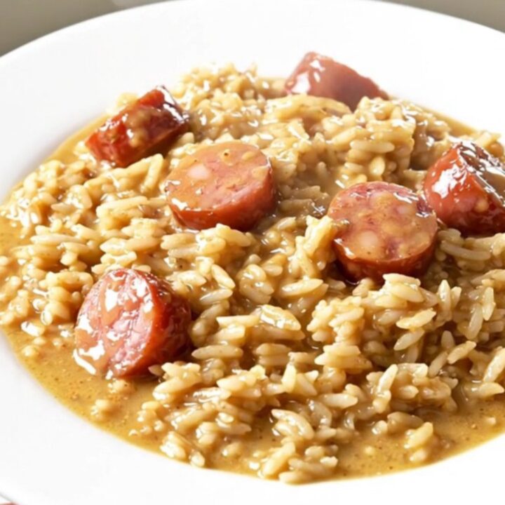 A close-up of a creamy Tuscan kielbasa and rice dish in a slow cooker on a white quartz countertop.