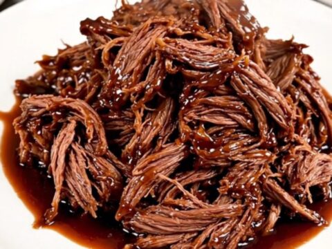 A glossy, shredded beef dish served on a white plate with a rich cherry-infused glaze.