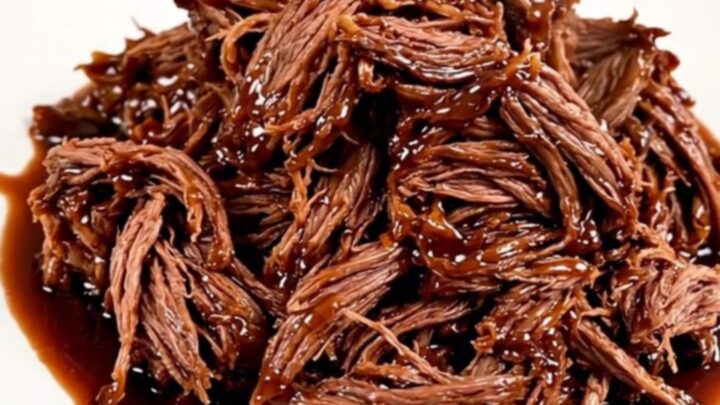 A glossy, shredded beef dish served on a white plate with a rich cherry-infused glaze.
