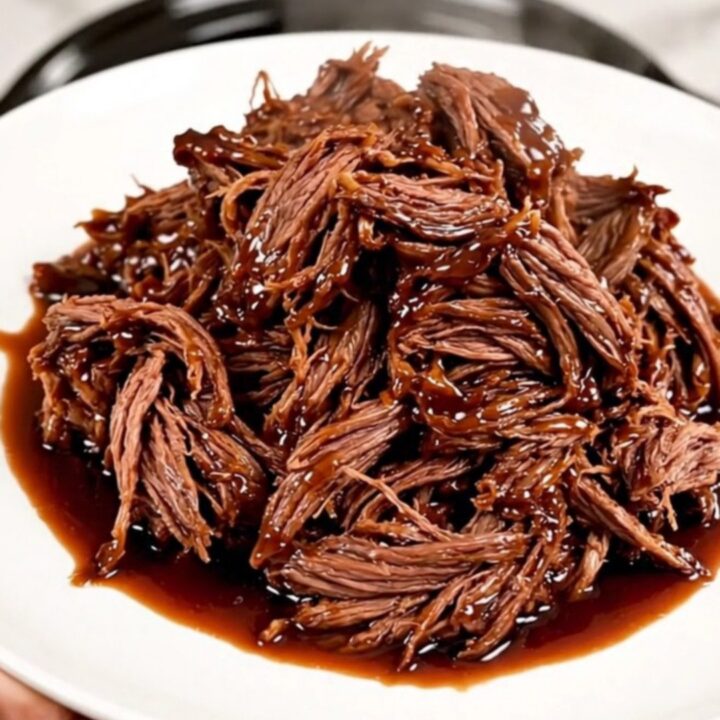 A glossy, shredded beef dish served on a white plate with a rich cherry-infused glaze.