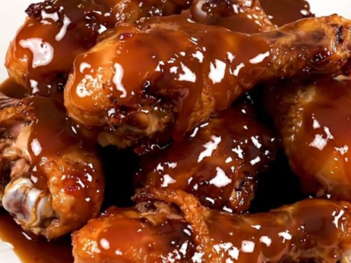 A top-down view of raw chicken drumsticks in a slow cooker with maple bourbon sauce and onions.