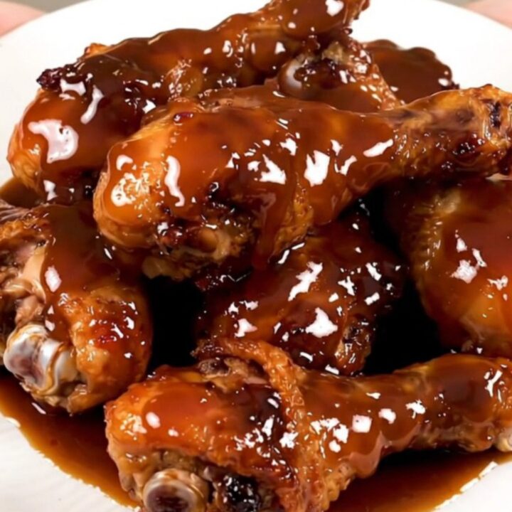 A top-down view of raw chicken drumsticks in a slow cooker with maple bourbon sauce and onions.