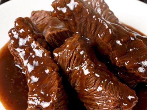 A top-down view of tender beef tips in a rich apple cider glaze served on a white plate.
