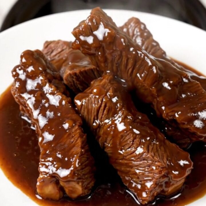 A top-down view of tender beef tips in a rich apple cider glaze served on a white plate.