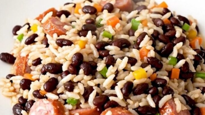 A close-up of a steaming, glossy dish of smoked sausage and black beans served on a white plate.