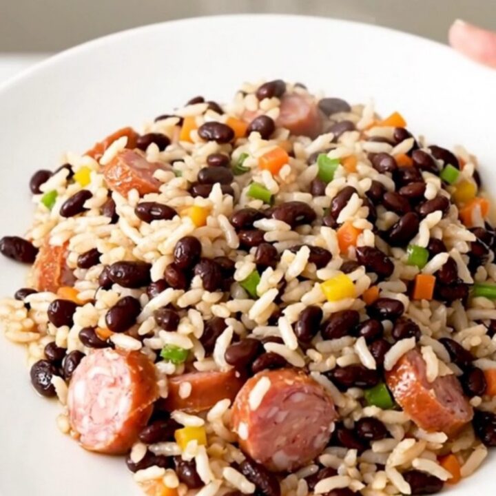 A close-up of a steaming, glossy dish of smoked sausage and black beans served on a white plate.