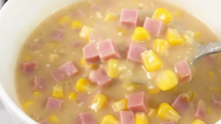 A steaming bowl of creamy ham and corn chowder served in a plain white bowl.