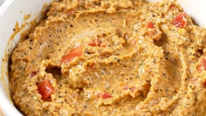 A warm, creamy, and glossy taco dip served in a white bowl with a spoon, showing a rich texture.