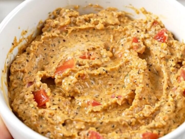 A warm, creamy, and glossy taco dip served in a white bowl with a spoon, showing a rich texture.