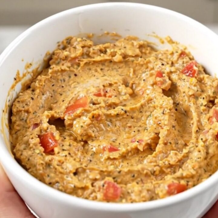 A warm, creamy, and glossy taco dip served in a white bowl with a spoon, showing a rich texture.