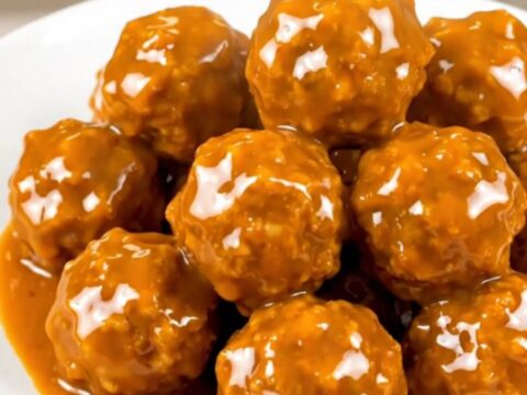 A close-up shot of glossy, orange-glazed chicken meatballs steaming on a white plate.