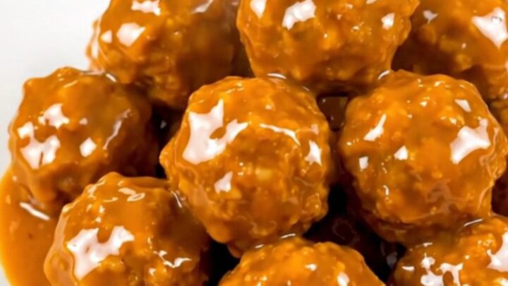 A close-up shot of glossy, orange-glazed chicken meatballs steaming on a white plate.