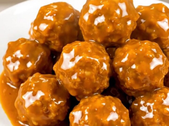 A close-up shot of glossy, orange-glazed chicken meatballs steaming on a white plate.