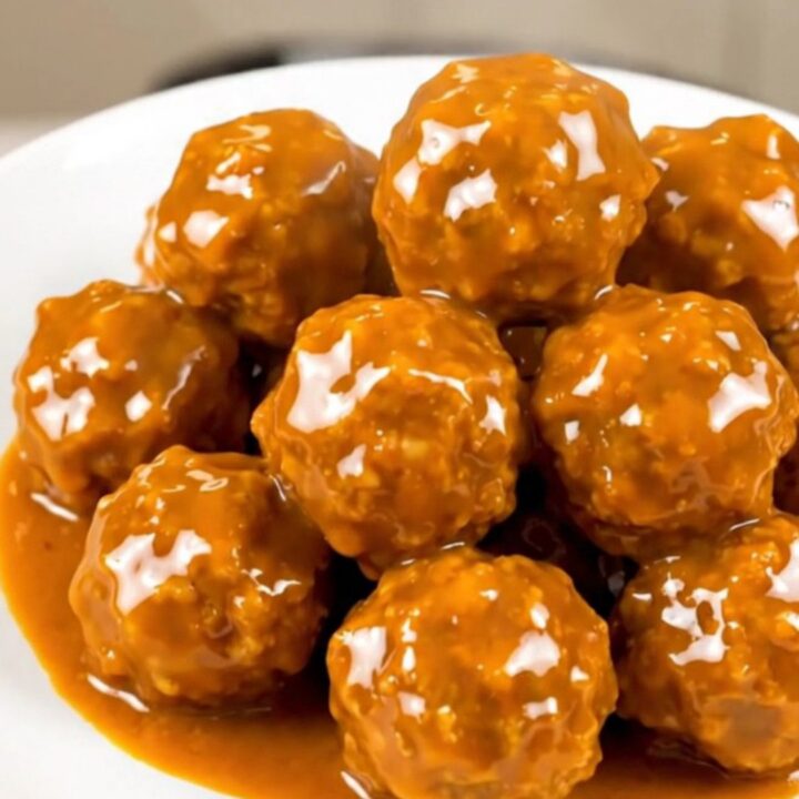 A close-up shot of glossy, orange-glazed chicken meatballs steaming on a white plate.