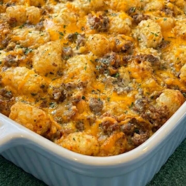 A golden-baked sausage and tater tot breakfast casserole in a white ribbed dish on a green cloth.