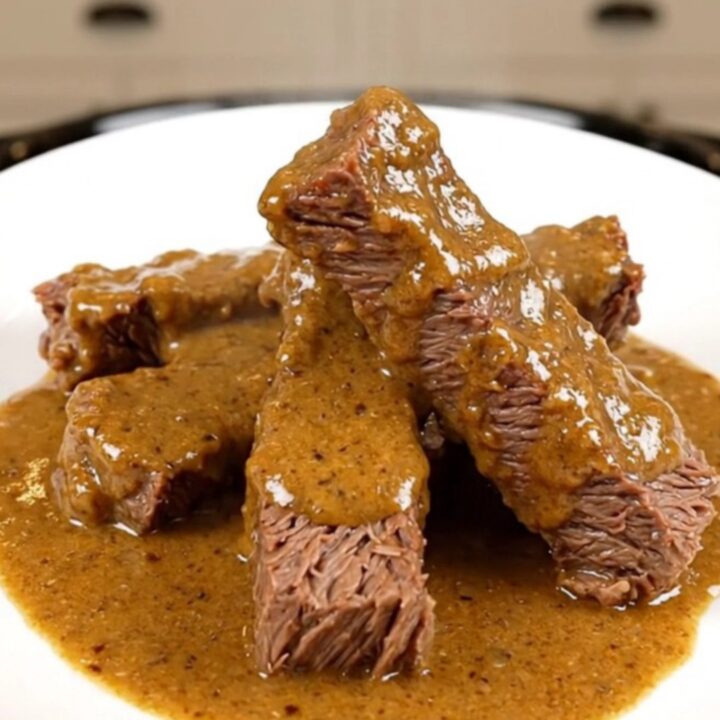 A slow cooker filled with tender beef tips in a rich, creamy sauce sitting on a kitchen counter.