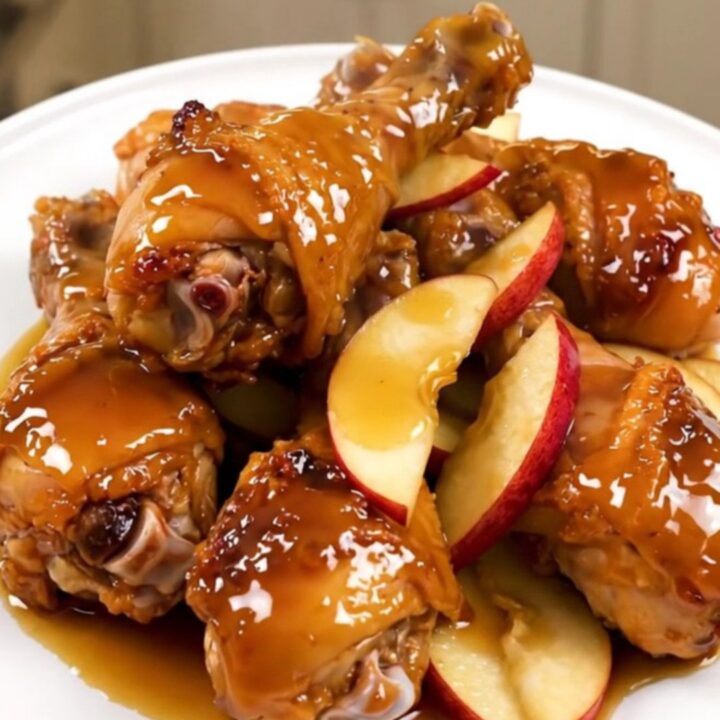 Slow cooker chicken drumsticks with apple slices and a rich glaze on a white plate.