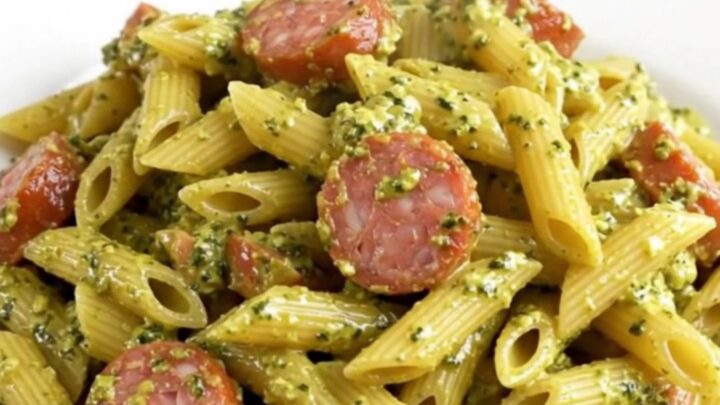 Creamy pesto Italian sausage penne served on a white plate with a rustic kitchen background.