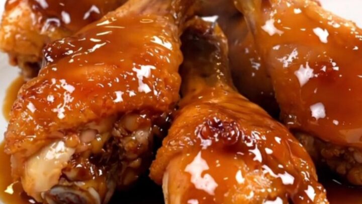 A close-up view of sticky honey garlic chicken drumsticks served on a white plate with a glossy glaze.